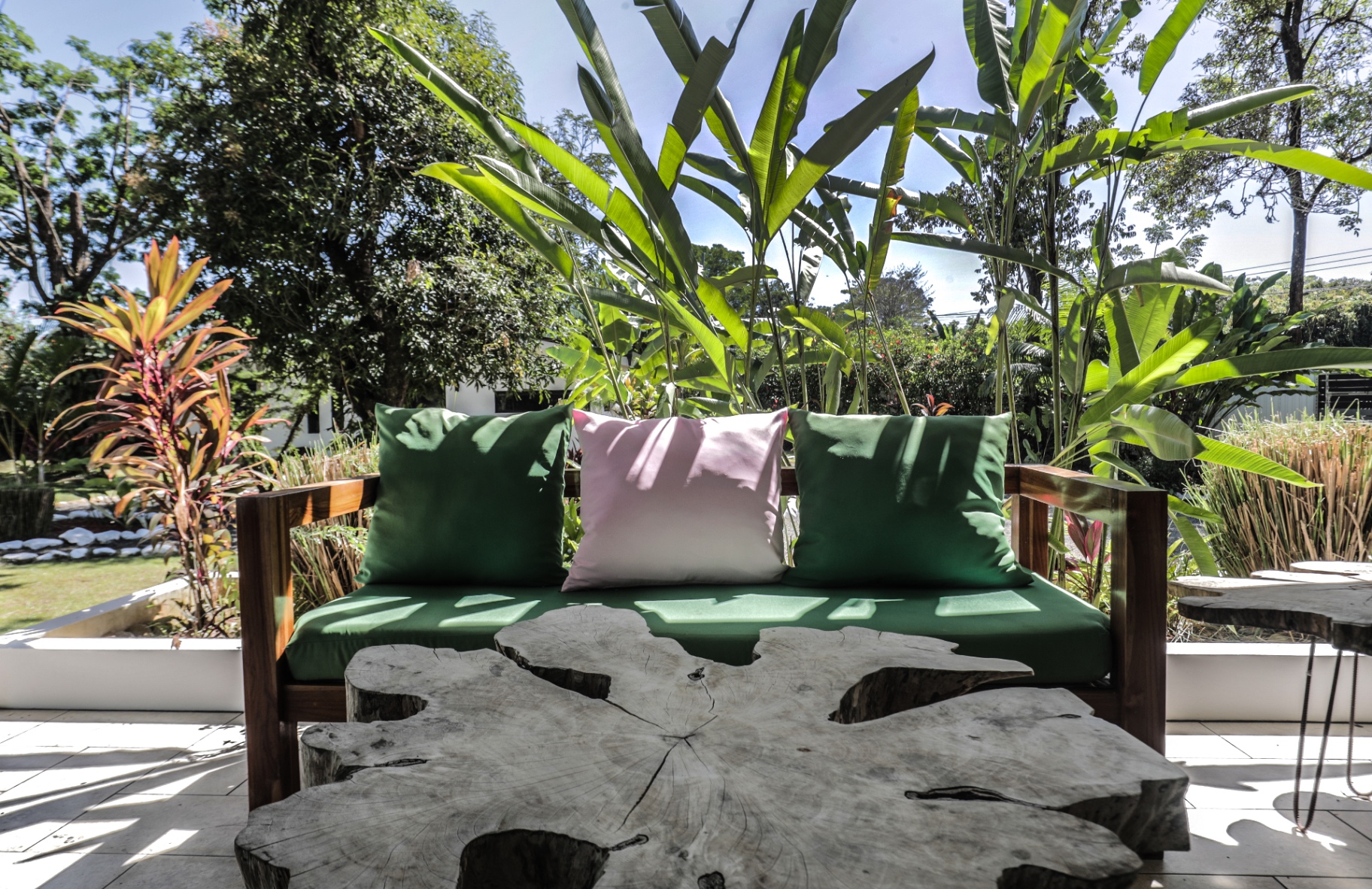 Wooden bench with green cushions beside a live-edge table in the tropical gardens