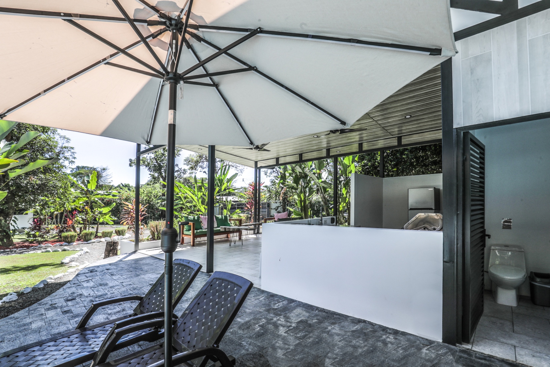 Pool loungers with a canvas umbrella beside the shared outdoor kitchen at The Retreat Uvita
