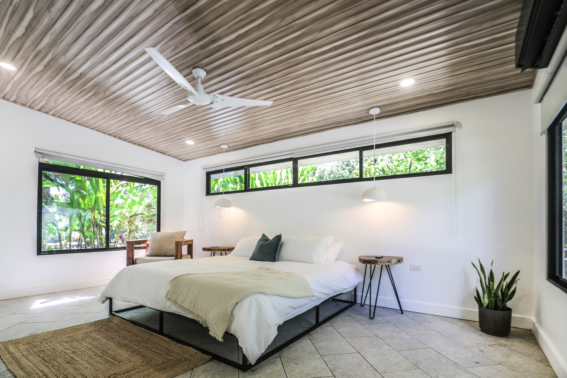 Spacious king bedroom with vaulted wood ceiling, jute rug, pendant lights and floor-to-ceiling garden window in Unit 4