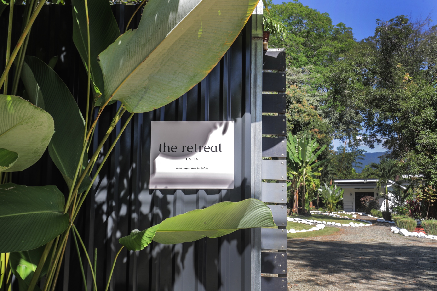 Gated entrance and gravel driveway of The Retreat Uvita with tropical foliage and mountain backdrop in Bahía Ballena
