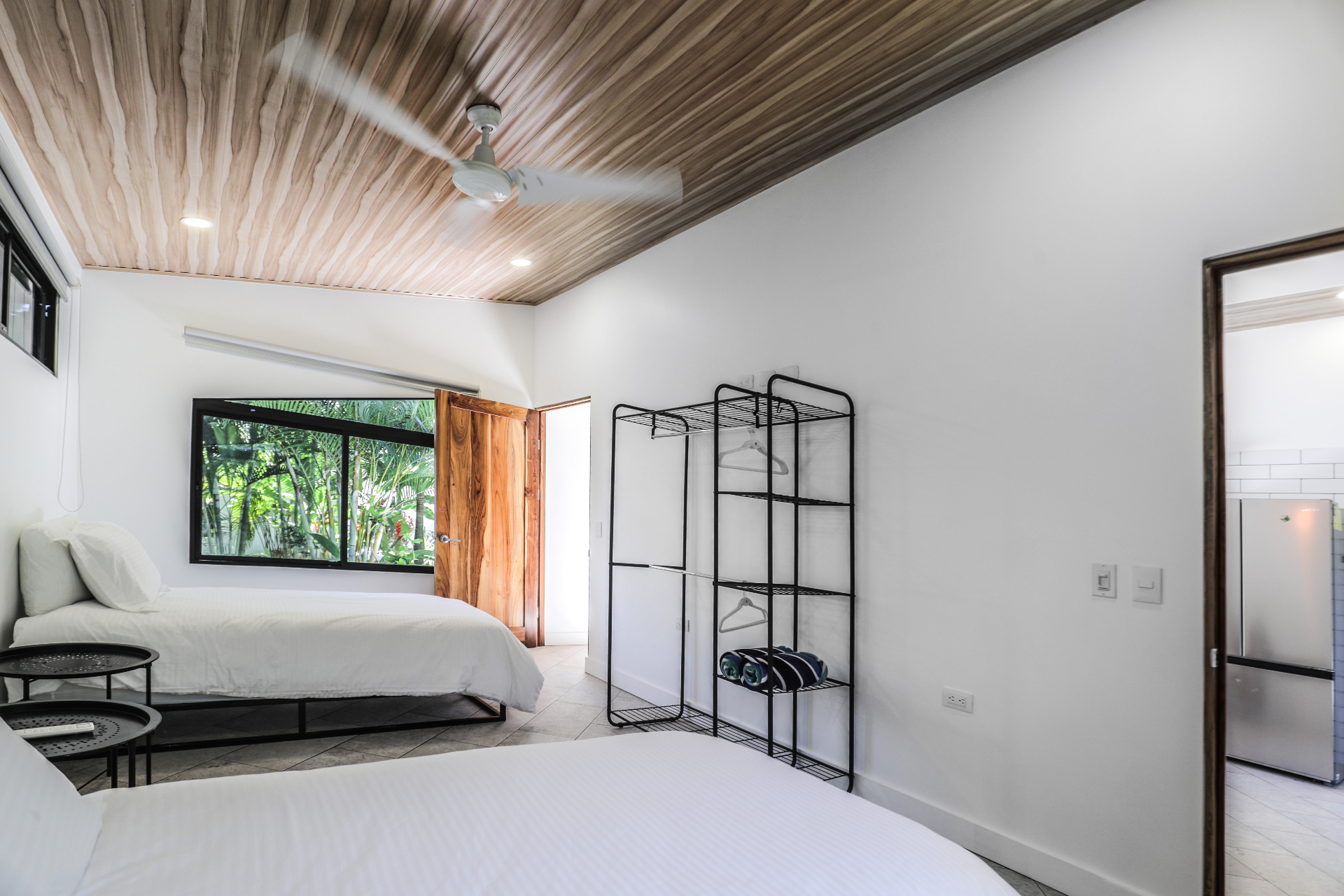 Second angle of the twin bedroom with garden window, open wood door and minimalist storage rack in Unit 4
