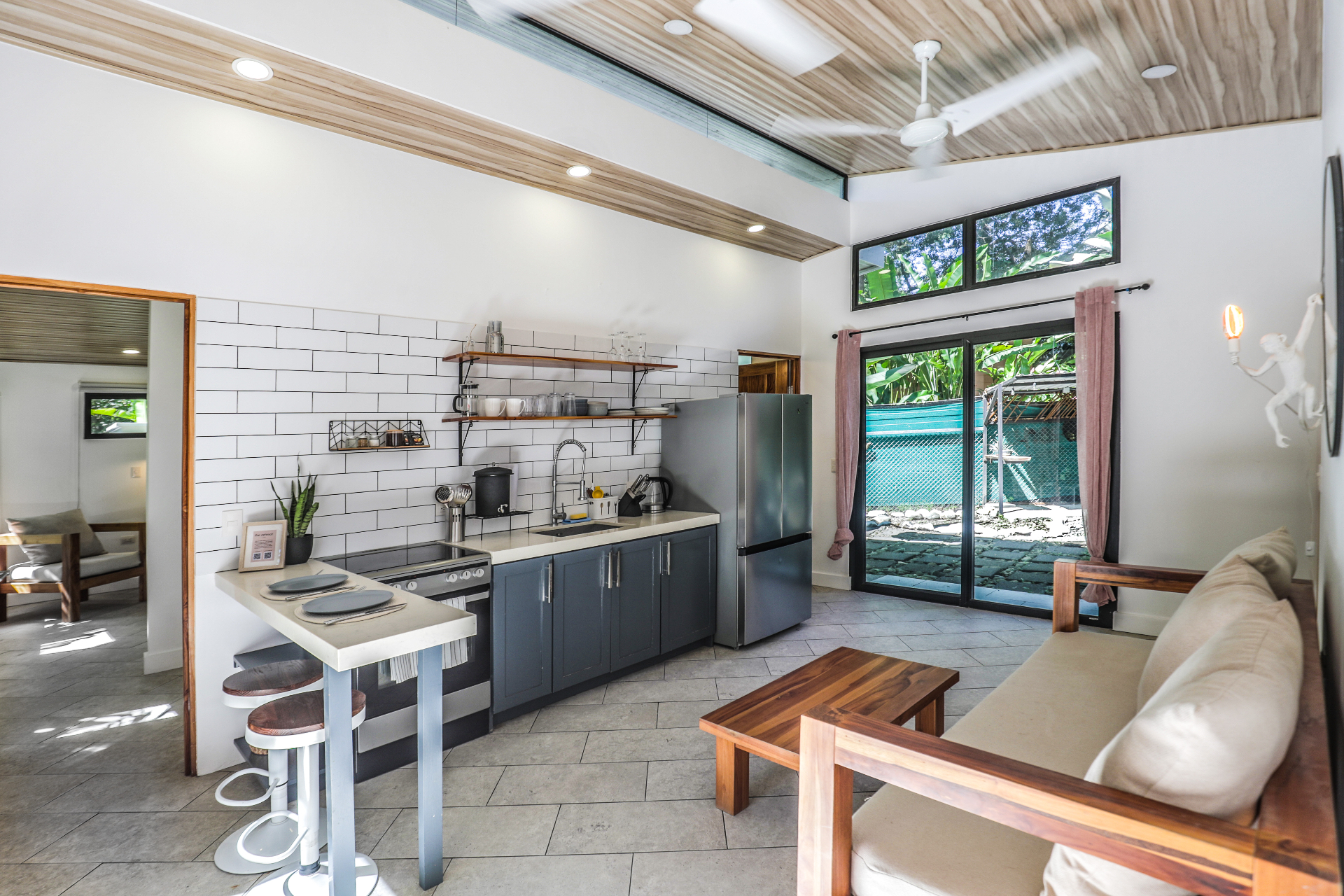 Open-plan living area and kitchen with sofa seating, breakfast bar, subway tile backsplash and garden-facing sliding doors in Unit 4